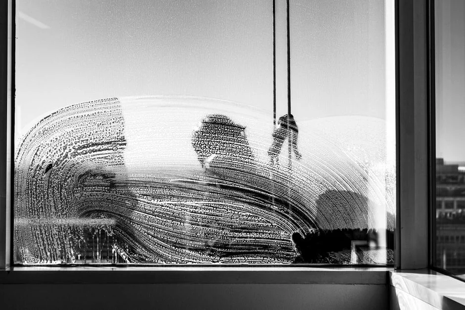 about-002 Black and white from below of man steeplejack in protective helmet with professional equipment cleaning glass wall of modern tower